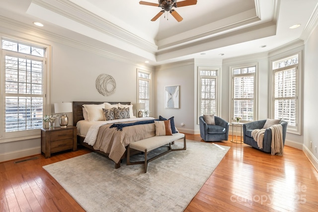 bedroom featuring light wood finished floors, a tray ceiling, and multiple windows