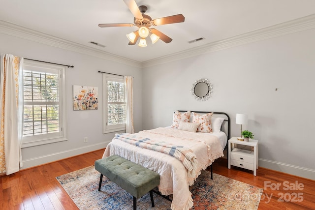 bedroom with crown molding, multiple windows, visible vents, and wood finished floors