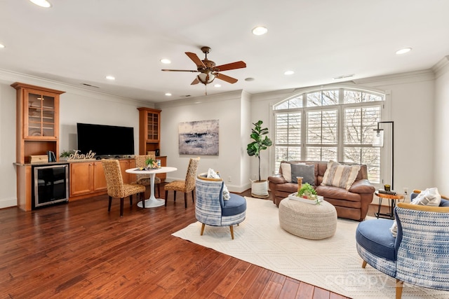 living room featuring beverage cooler, dark wood finished floors, ceiling fan, ornamental molding, and recessed lighting