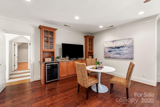 dining area with dark wood-type flooring, beverage cooler, visible vents, and ornamental molding