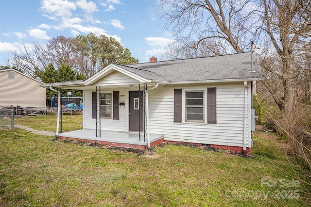 bungalow-style home featuring covered porch, fence, a front lawn, a trampoline, and a chimney