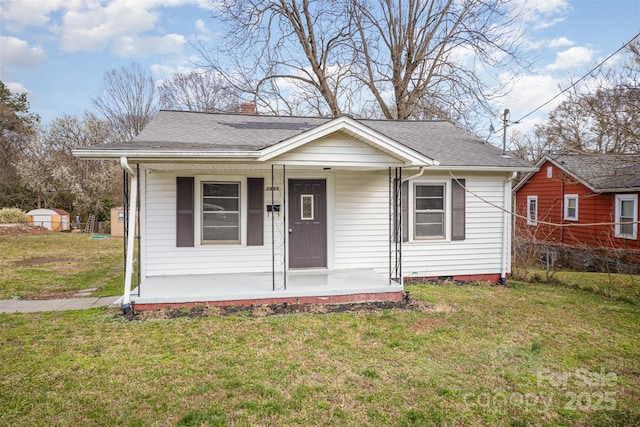 bungalow-style house with covered porch, roof with shingles, a front yard, and a chimney