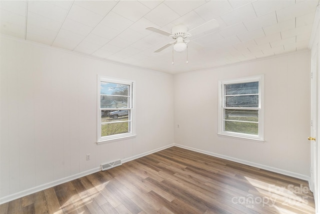 spare room with crown molding, visible vents, a ceiling fan, wood finished floors, and baseboards