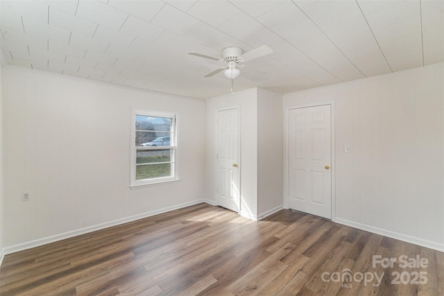 empty room featuring ornamental molding, wood finished floors, a ceiling fan, and baseboards