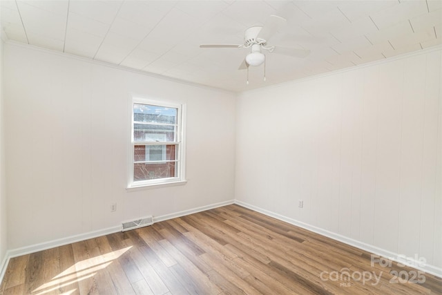 spare room with a ceiling fan, visible vents, crown molding, and wood finished floors