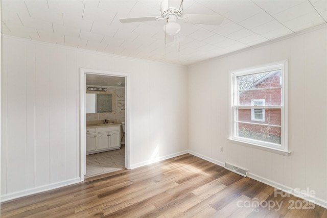 spare room with light wood-style flooring, a sink, a ceiling fan, visible vents, and baseboards