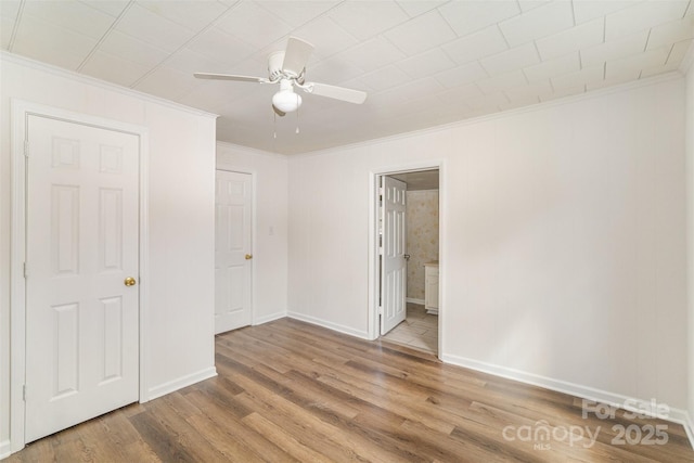 unfurnished bedroom featuring connected bathroom, a ceiling fan, baseboards, light wood finished floors, and crown molding