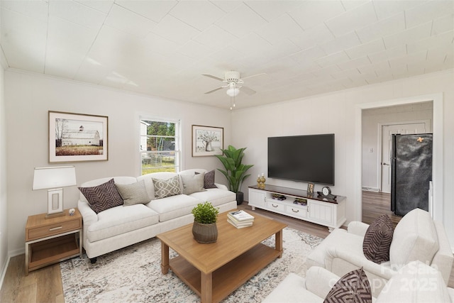 living room featuring a ceiling fan, ornamental molding, baseboards, and wood finished floors