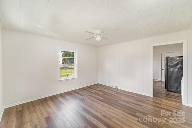 spare room featuring crown molding, visible vents, a ceiling fan, wood finished floors, and baseboards