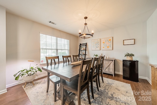 dining space featuring an inviting chandelier, baseboards, visible vents, and wood finished floors