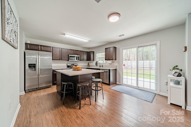 kitchen with stainless steel appliances, dark brown cabinets, a breakfast bar area, and light countertops