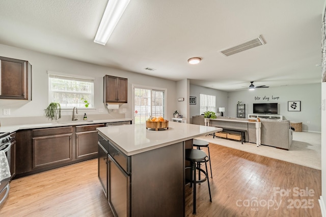 kitchen featuring dark brown cabinetry, visible vents, a kitchen breakfast bar, a center island, and a sink