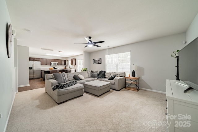 living area featuring light carpet, a ceiling fan, and baseboards