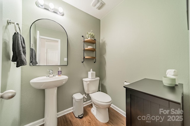 bathroom with toilet, visible vents, baseboards, and wood finished floors