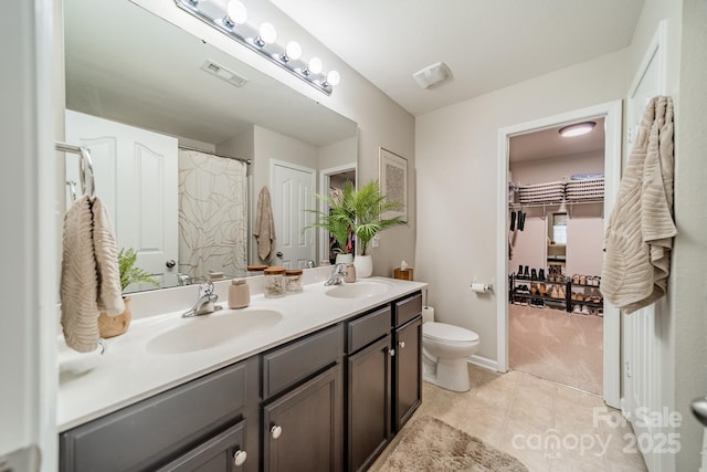 bathroom with toilet, double vanity, a sink, and tile patterned floors