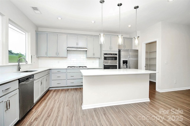 kitchen with under cabinet range hood, stainless steel appliances, a sink, gray cabinets, and decorative backsplash