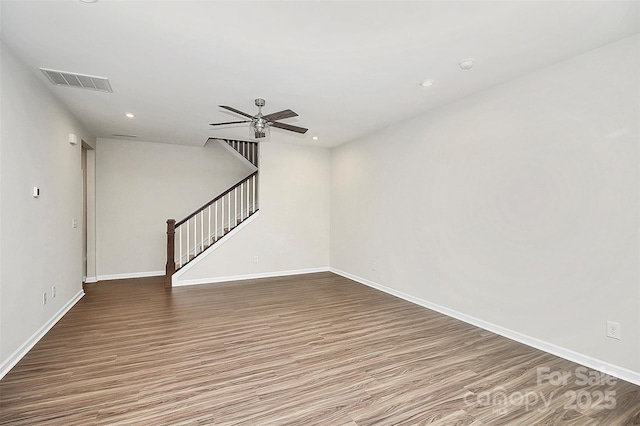 spare room with wood finished floors, a ceiling fan, visible vents, stairs, and baseboards