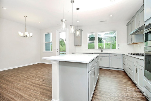 kitchen featuring a center island, gray cabinets, backsplash, a sink, and wood finished floors