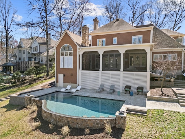 back of house featuring roof with shingles, a chimney, a sunroom, an outdoor pool, and a patio