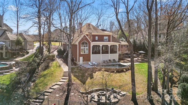 rear view of property featuring an outdoor fire pit, stairway, a sunroom, brick siding, and a chimney