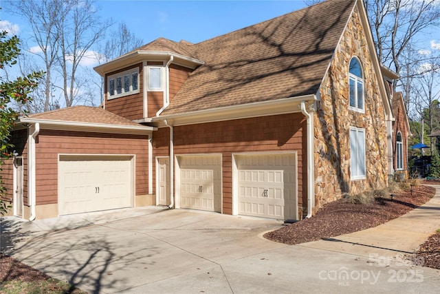view of front of property with concrete driveway, an attached garage, stone siding, and roof with shingles