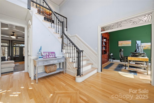 stairway with a ceiling fan, a high ceiling, wood finished floors, and crown molding