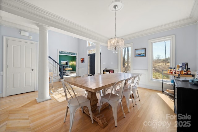 dining area featuring stairway, an inviting chandelier, crown molding, wainscoting, and decorative columns