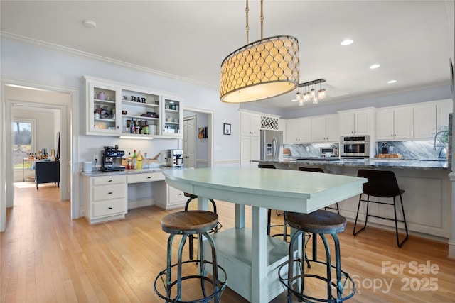 kitchen featuring light wood-style flooring, a kitchen breakfast bar, appliances with stainless steel finishes, and ornamental molding