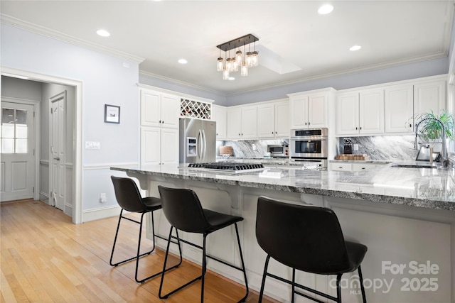 kitchen featuring light wood-type flooring, a sink, white cabinetry, appliances with stainless steel finishes, and a peninsula