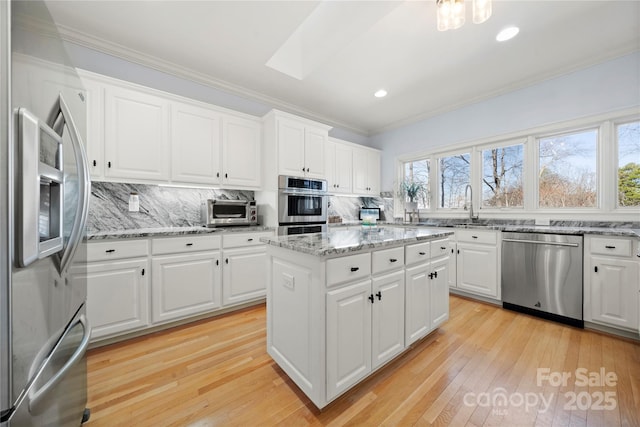 kitchen with light wood-type flooring, backsplash, a center island, appliances with stainless steel finishes, and a skylight