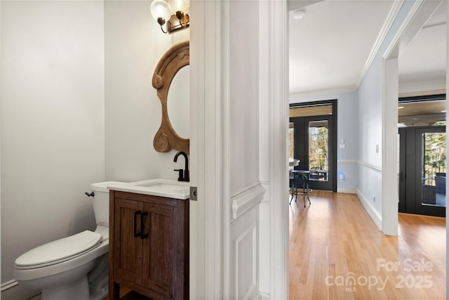 half bathroom with toilet, ornamental molding, wood finished floors, baseboards, and vanity