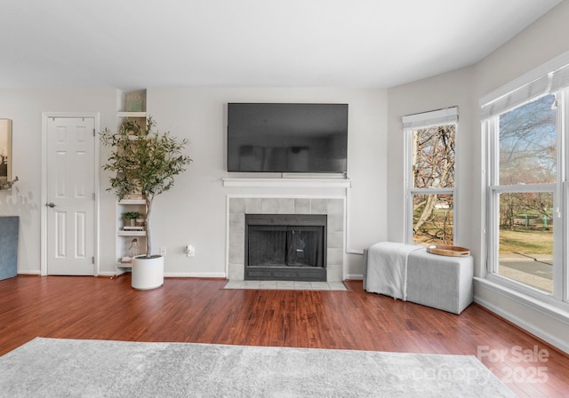 unfurnished living room featuring a tiled fireplace, plenty of natural light, and wood finished floors