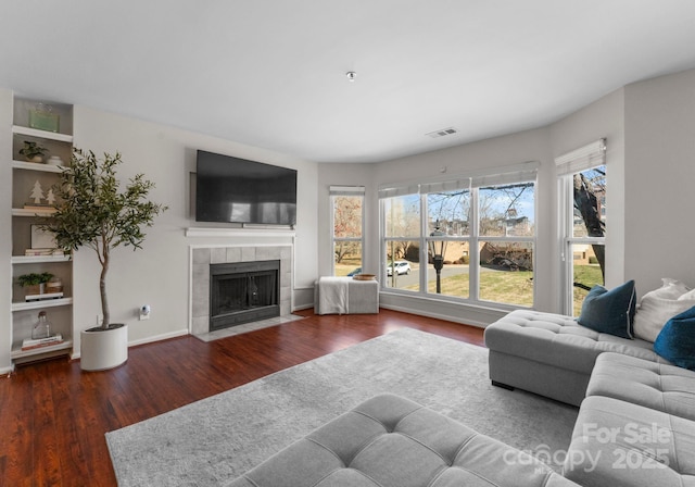 living area with a tiled fireplace, visible vents, baseboards, and wood finished floors