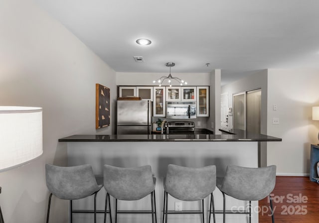 kitchen with dark wood-type flooring, a kitchen breakfast bar, appliances with stainless steel finishes, a peninsula, and glass insert cabinets