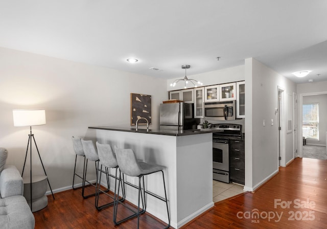 kitchen with a sink, dark countertops, wood finished floors, appliances with stainless steel finishes, and a peninsula