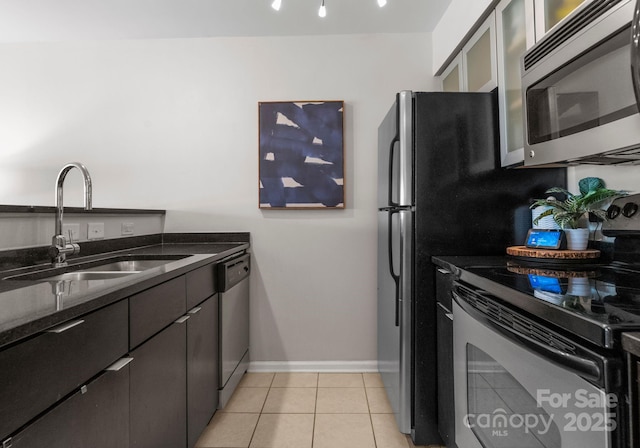 kitchen with glass insert cabinets, light tile patterned floors, dark stone countertops, appliances with stainless steel finishes, and a sink