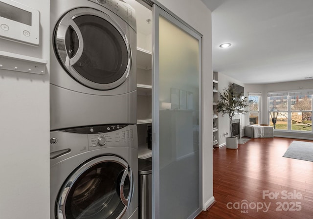 laundry area featuring wood finished floors, recessed lighting, a fireplace, stacked washer / dryer, and laundry area