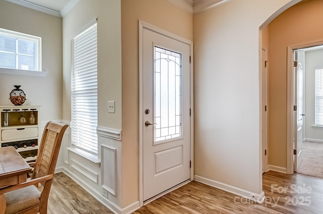 entryway with arched walkways, ornamental molding, baseboards, and light wood-style floors