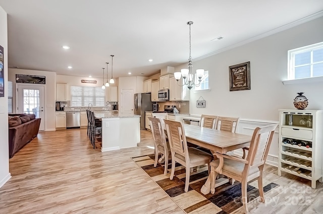 dining space featuring crown molding, an inviting chandelier, light wood-style flooring, and recessed lighting