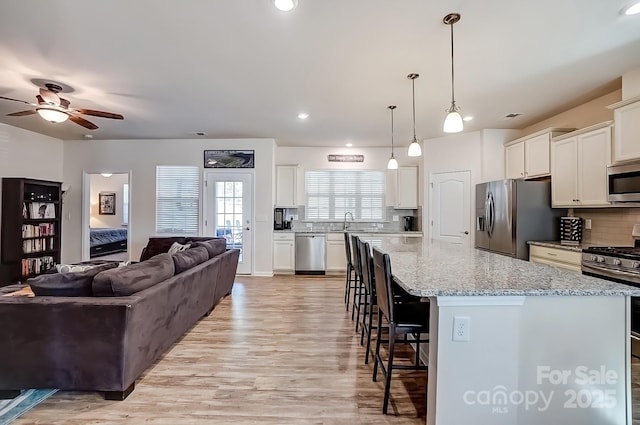 kitchen with a sink, a kitchen breakfast bar, open floor plan, appliances with stainless steel finishes, and tasteful backsplash