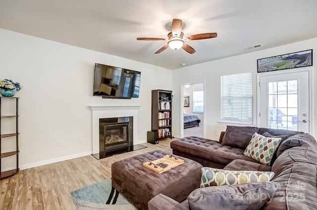 living room with visible vents, light wood-style flooring, a fireplace with flush hearth, ceiling fan, and baseboards