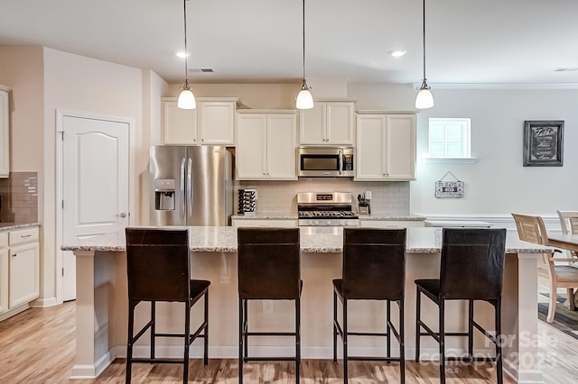 kitchen with a breakfast bar area, white cabinetry, appliances with stainless steel finishes, decorative backsplash, and pendant lighting