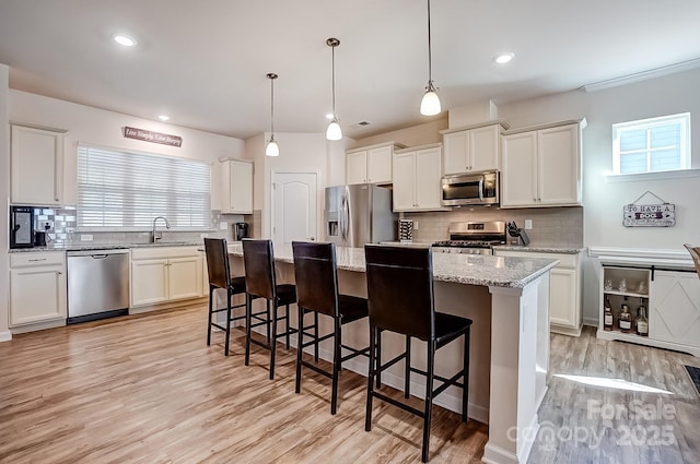 kitchen with appliances with stainless steel finishes, white cabinetry, a kitchen island, a sink, and a kitchen bar