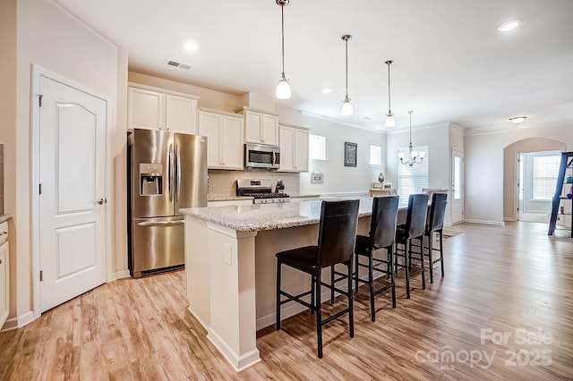 kitchen with arched walkways, a large island, stainless steel appliances, visible vents, and decorative backsplash