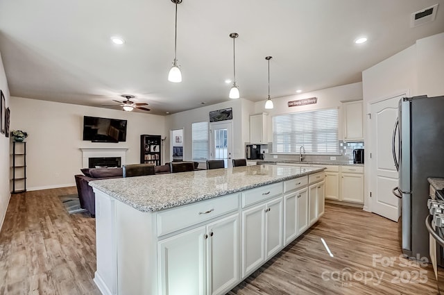 kitchen with visible vents, a kitchen island, freestanding refrigerator, a fireplace, and white cabinetry