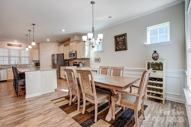 dining area featuring a notable chandelier, a wainscoted wall, visible vents, light wood-style floors, and crown molding