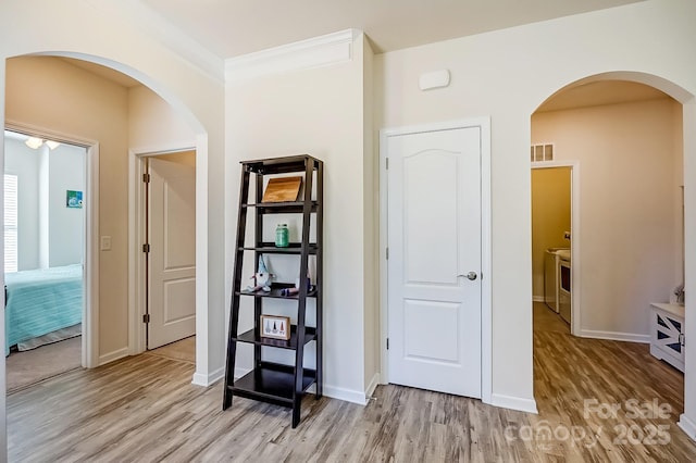 corridor with arched walkways, washing machine and clothes dryer, visible vents, light wood-type flooring, and baseboards