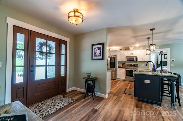 interior space featuring appliances with stainless steel finishes, wood finished floors, a kitchen bar, white cabinetry, and a sink