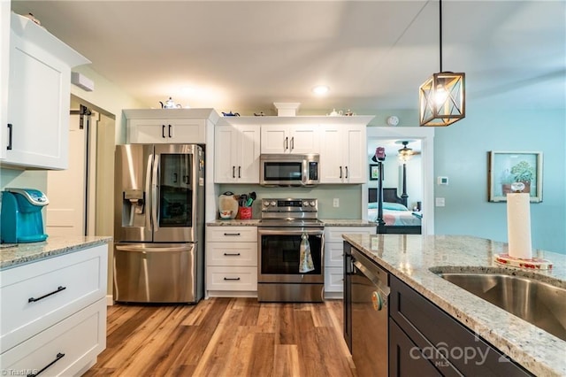 kitchen featuring light stone counters, stainless steel appliances, white cabinetry, light wood-type flooring, and pendant lighting