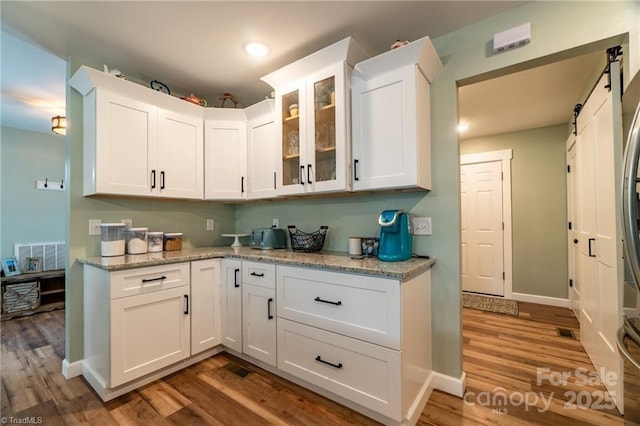 kitchen featuring a barn door, wood finished floors, baseboards, white cabinets, and glass insert cabinets